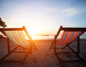 Two chairs on the shoreline of the beach facing the ocean with view looking towards the sun raising